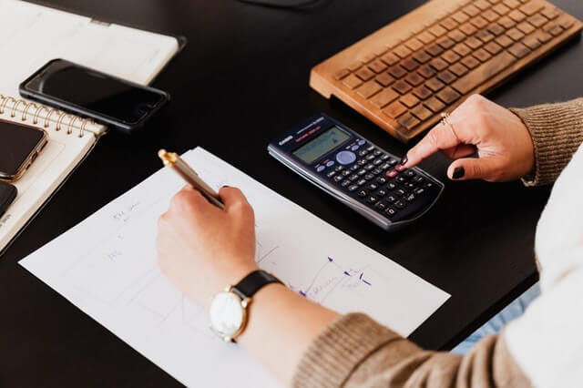 Início crop woman using calculator and taking notes on paper
